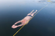 氷の張った湖で透き通る氷の下をフリーダイビングする男性
